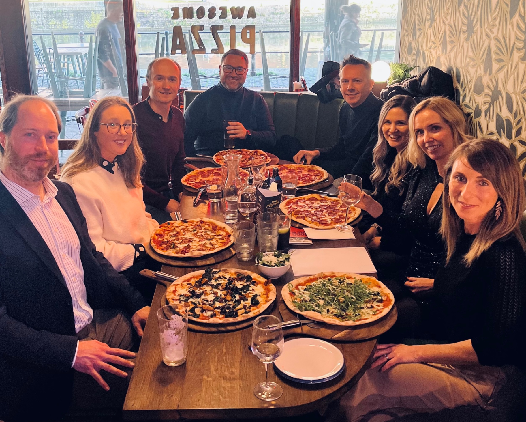 Founders Lounge members around a long table of pizzas on Bristol harbourside